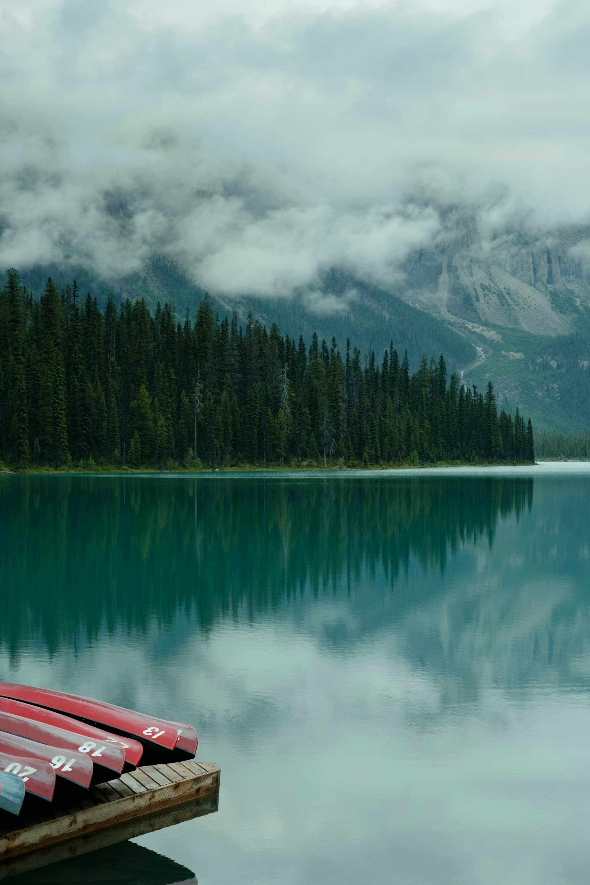 An emerald mountain lake, canoes stacked on the dock, misty peaks behind