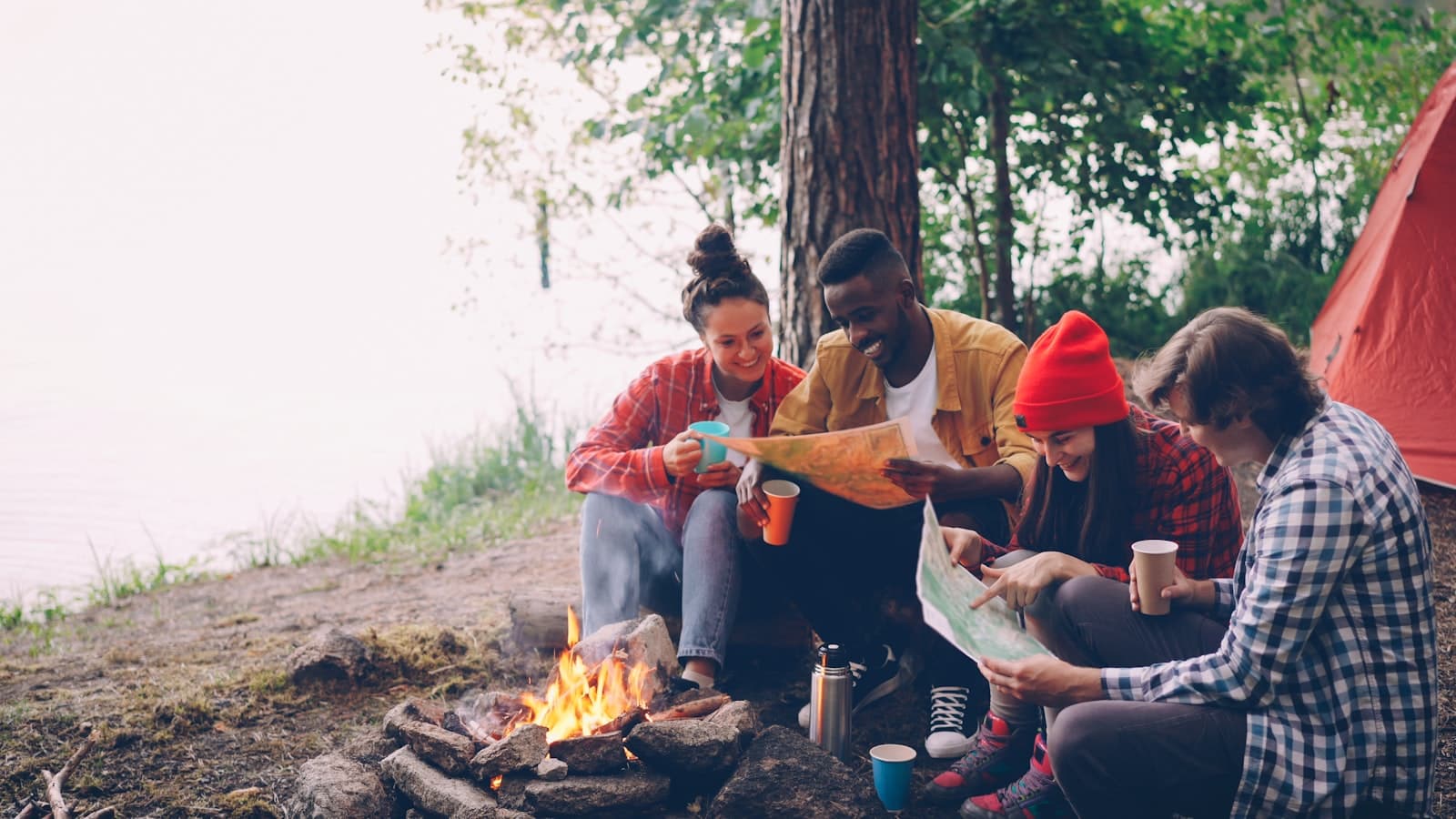 Friends gathered around a campfire by the lake at dusk