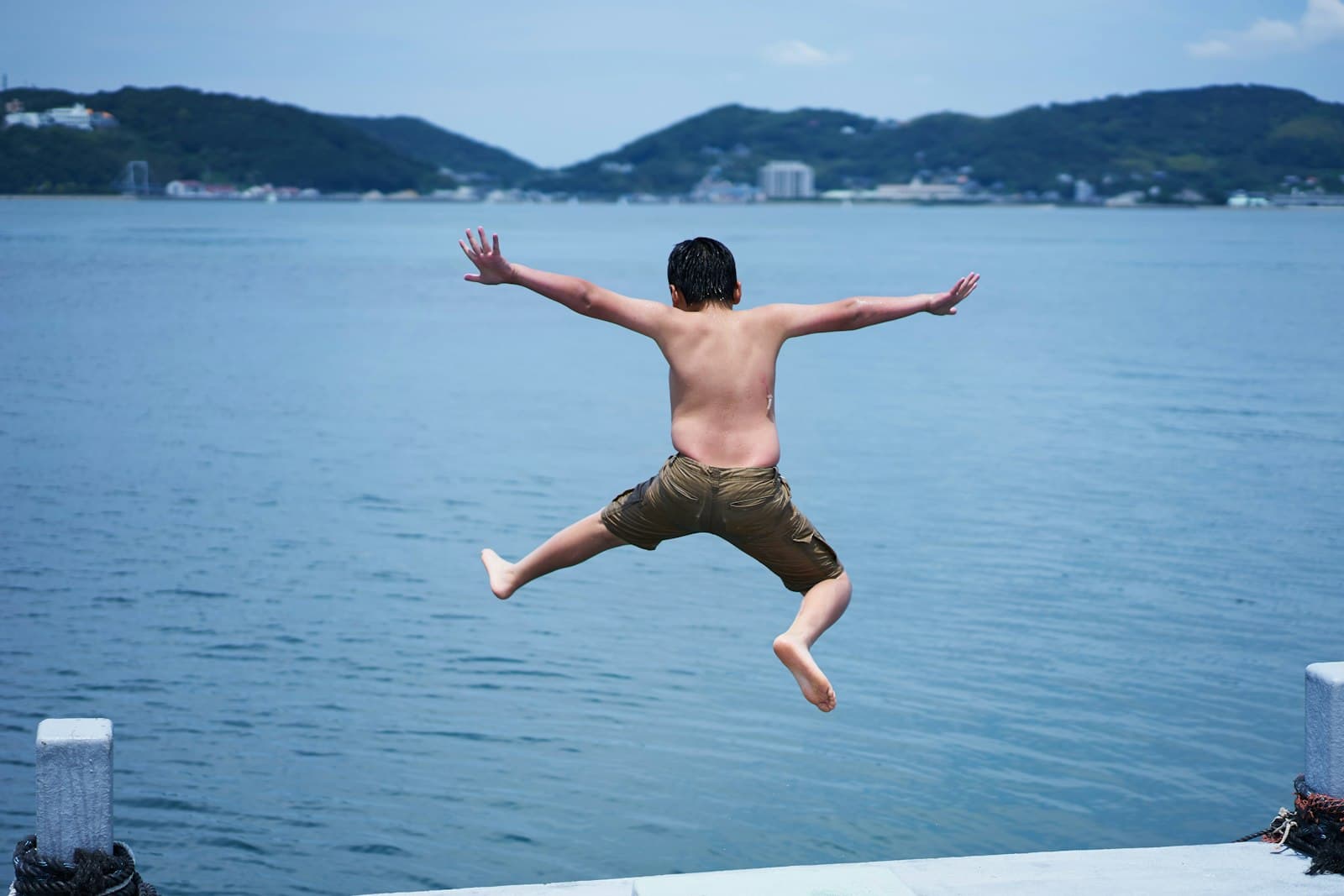 A boy mid-jump off the dock into the lake